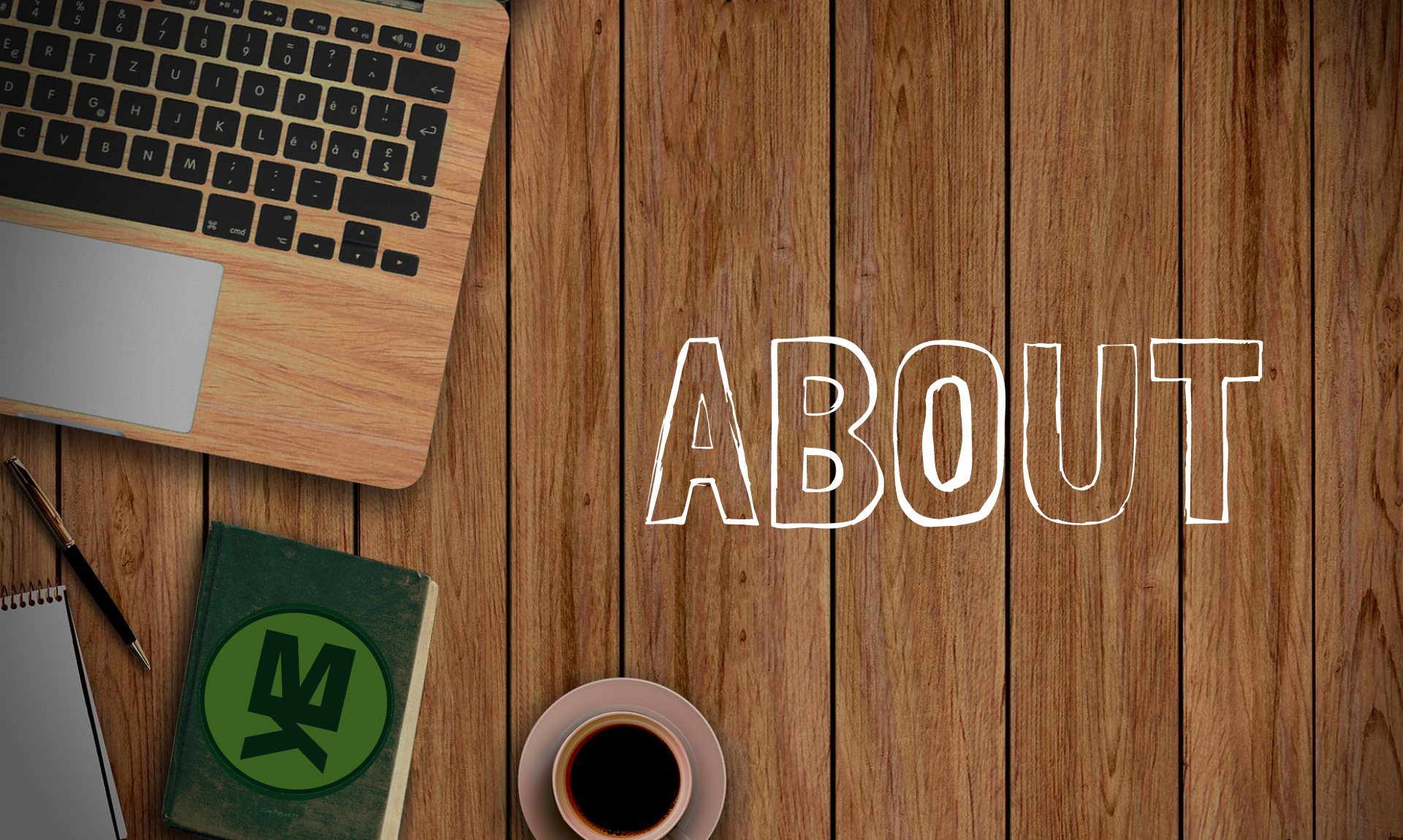 An overhead view of a wooden surfaced open laptop, pen, notebook and coffee resting on a wooden surfaced table. The word "About" is written next to these items.