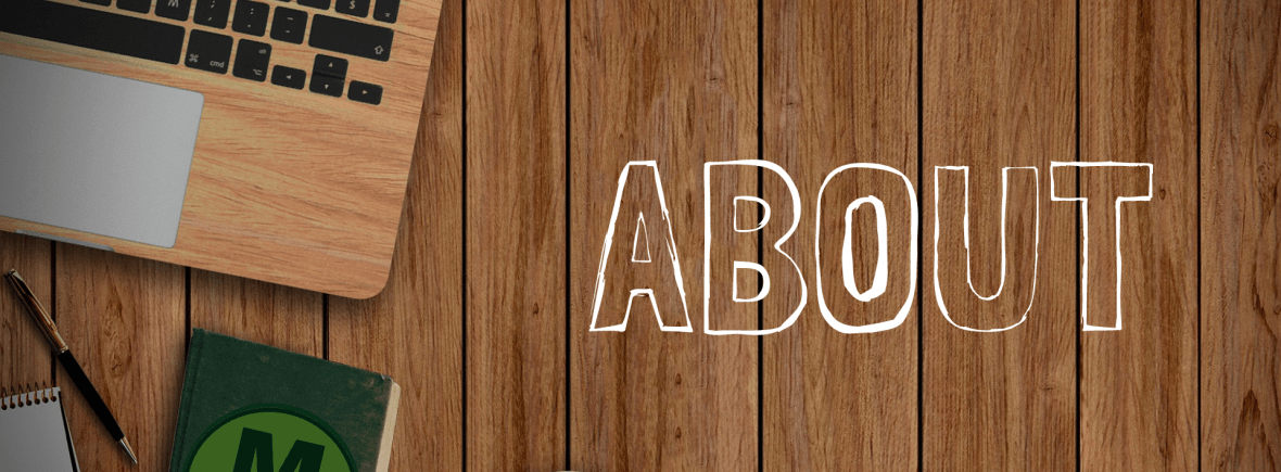 An overhead view of a wooden surfaced open laptop, pen, notebook and coffee resting on a wooden surfaced table. The word "About" is written next to these items.